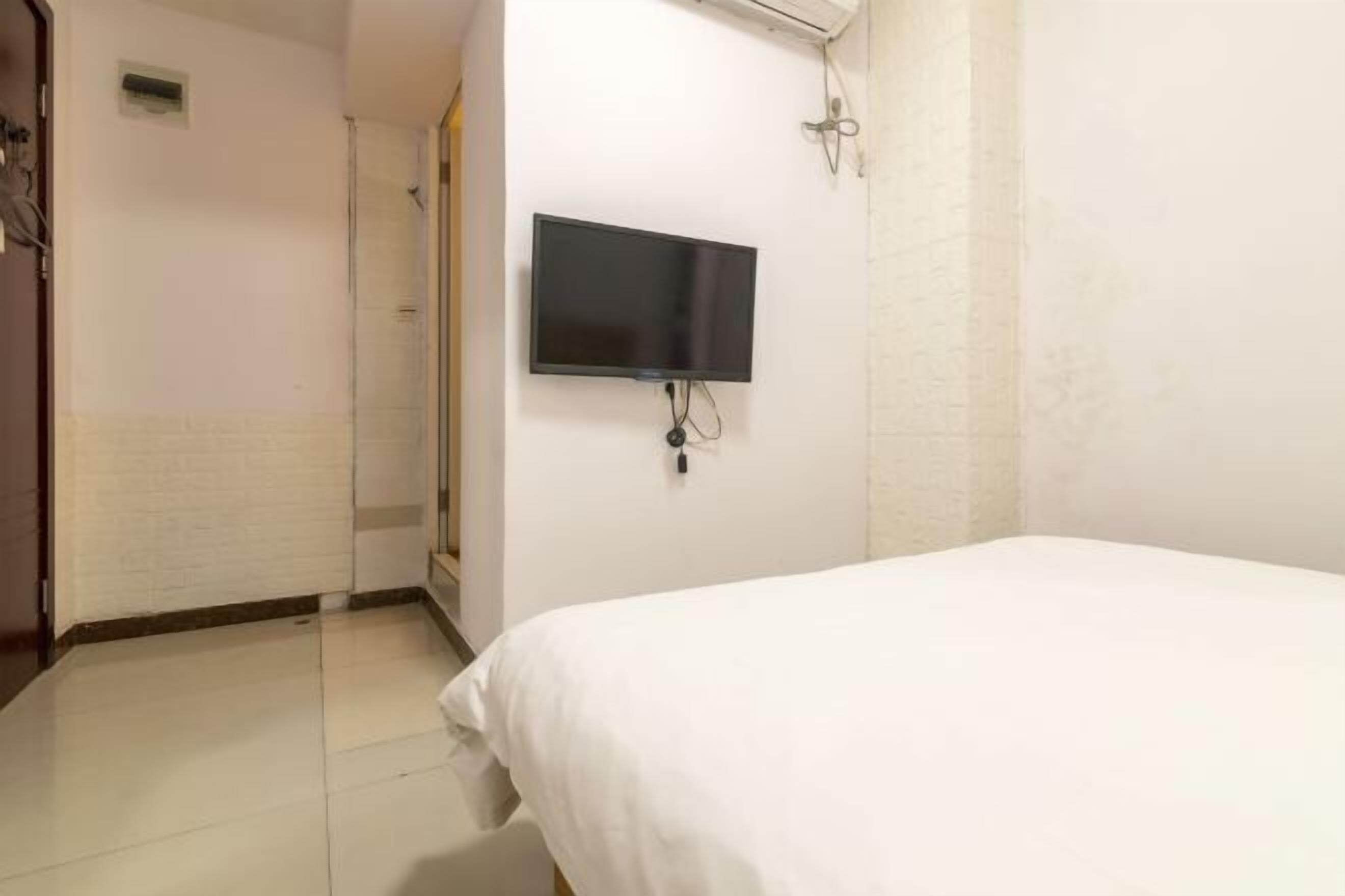 A hotel room with a bed, a television mounted on the wall, and a shower area.