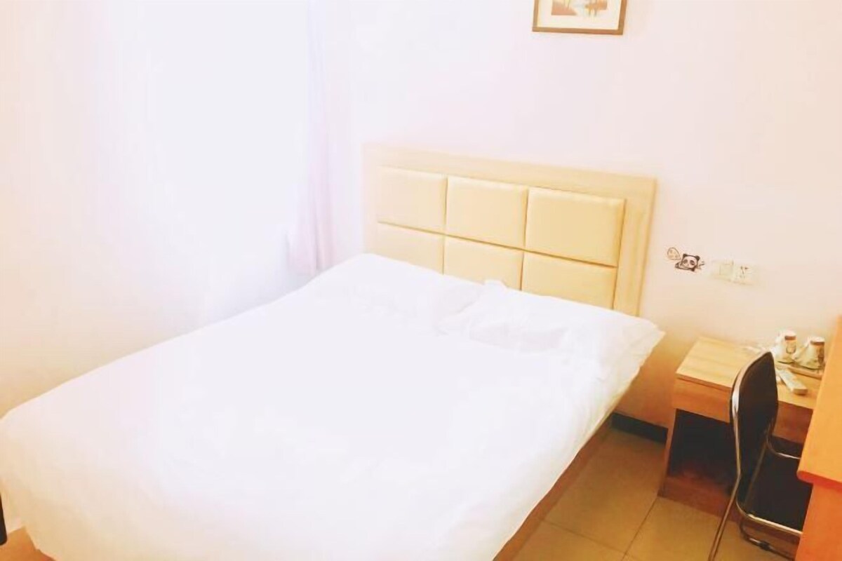 Ein Hotelzimmer mit einem Einzelbett, einem Nachttisch, einem Sessel und einem kleinen Schreibtisch mit einer Lampe.