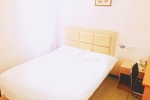 Ein Hotelzimmer mit einem Einzelbett, einem Nachttisch, einem Sessel und einem kleinen Schreibtisch mit einer Lampe.