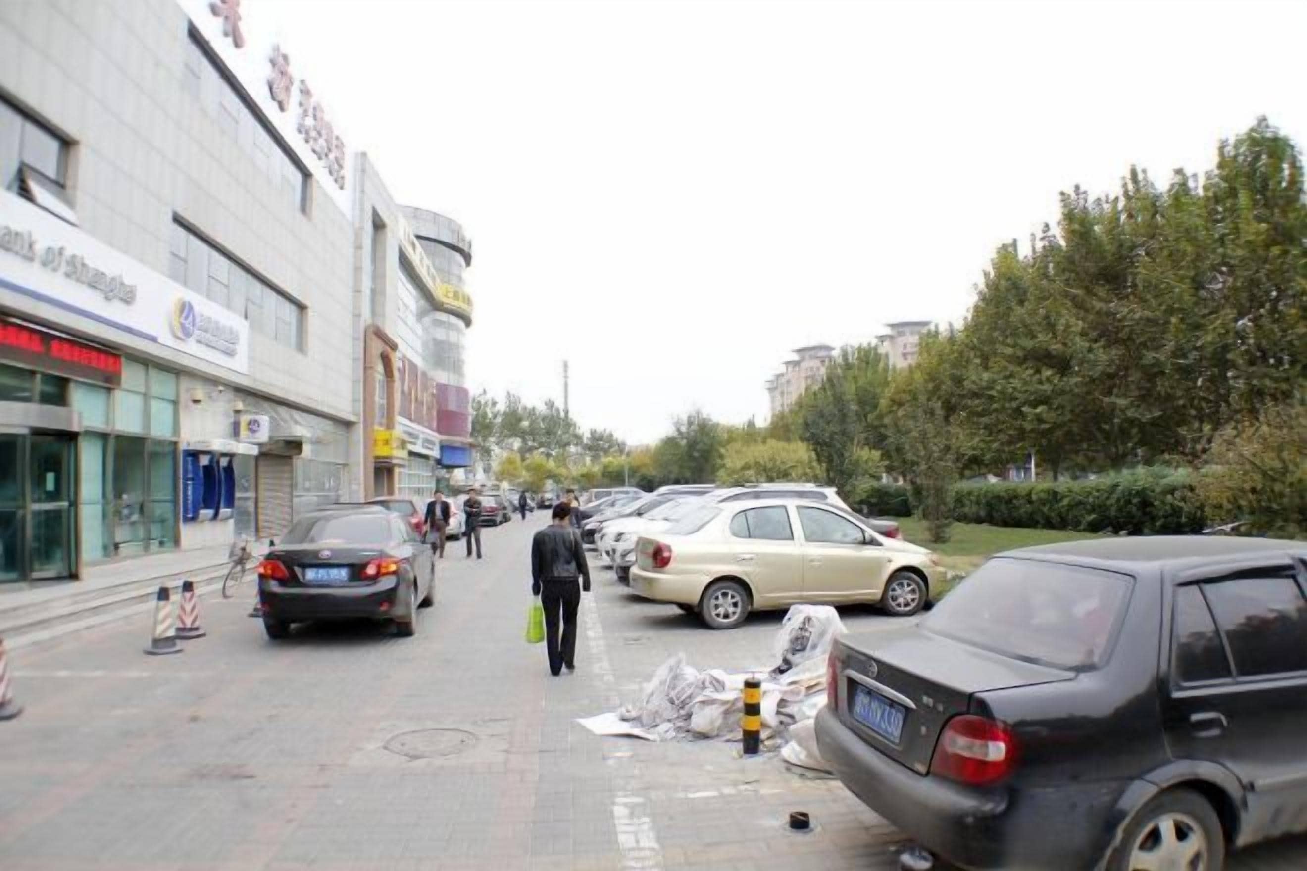 A street with parked cars, a pedestrian, and buildings with signage.