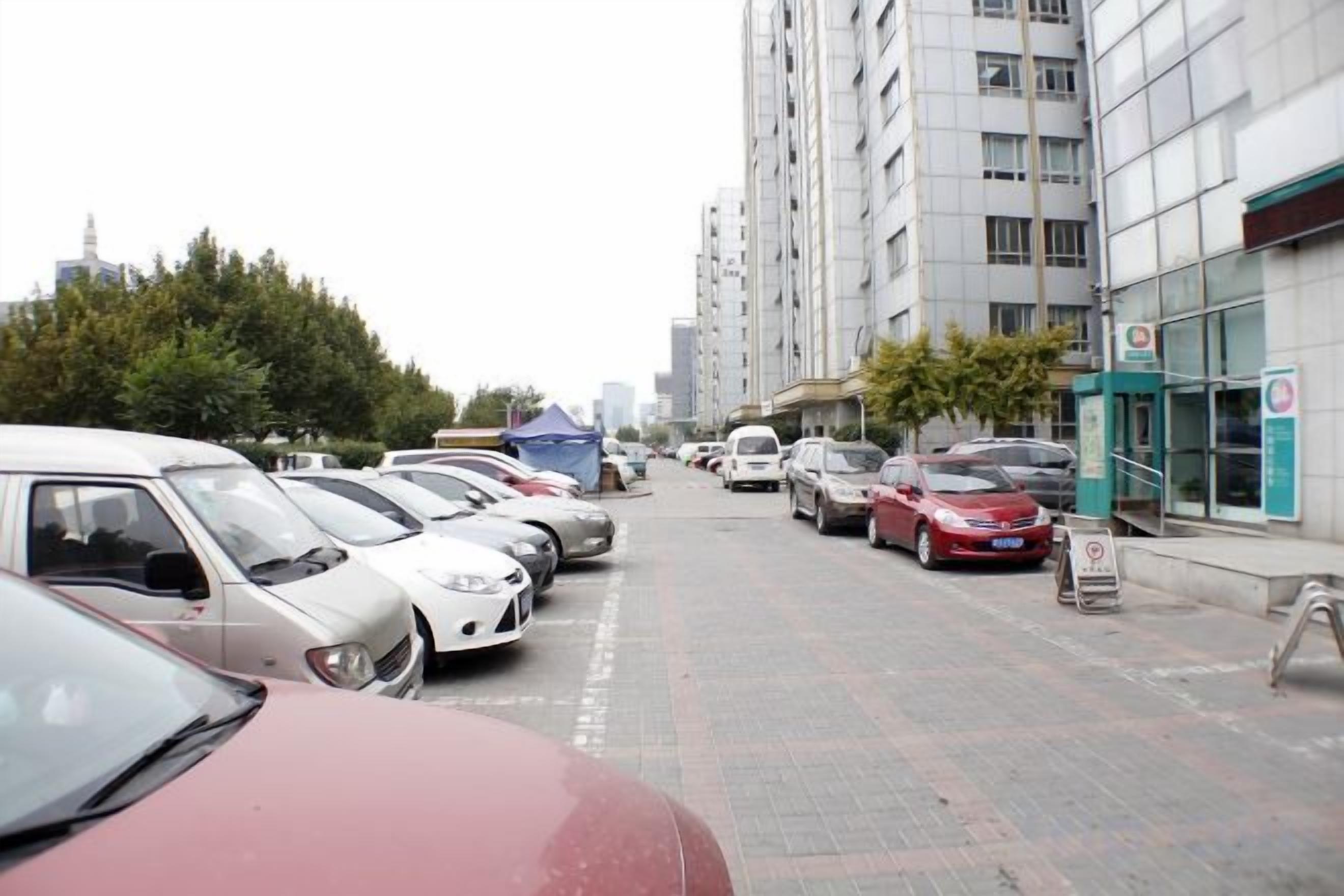 Un estacionamiento con varios coches aparcados en filas, junto a un edificio con un letrero.