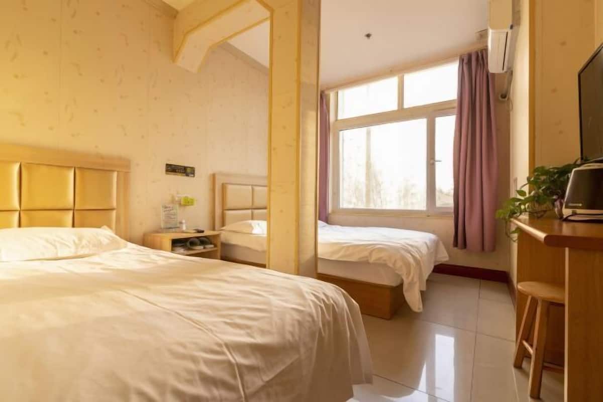 Ett hotellrum med två sängar, ett skrivbord med en stol, en TV och ett fönster med gardiner.