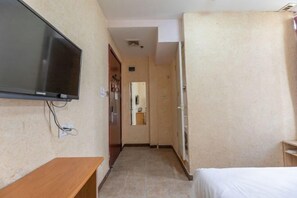 Ein Hotelzimmer mit Bett, Wandfernseher, einer Holzbank und einer Tür zu einem Badezimmer.