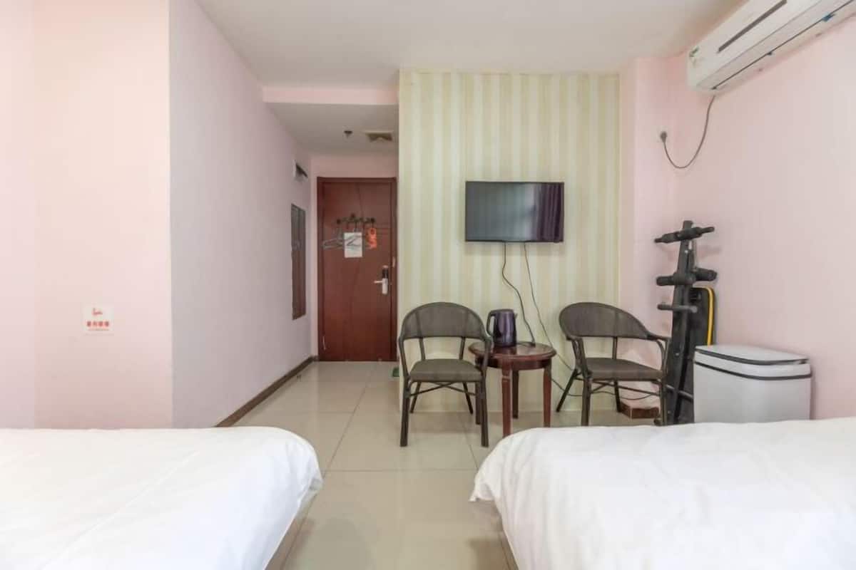 Ett hotellrum med två sängar, en tv, ett litet bord med en stol och en luftkonditioneringsanläggning.