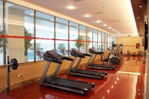 A gym with treadmills aligned against a wall with large windows, a weight bench, and exercise equipment.