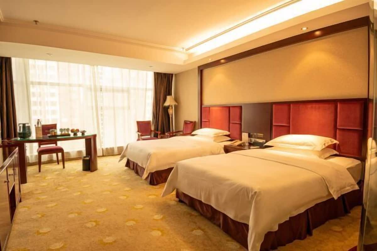 Habitación de hotel con dos camas, un escritorio, una silla y un amplio ventanal con cortinas.