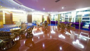 A spacious lobby with a polished wooden floor, wicker furniture, and a large seating area with purple couches.