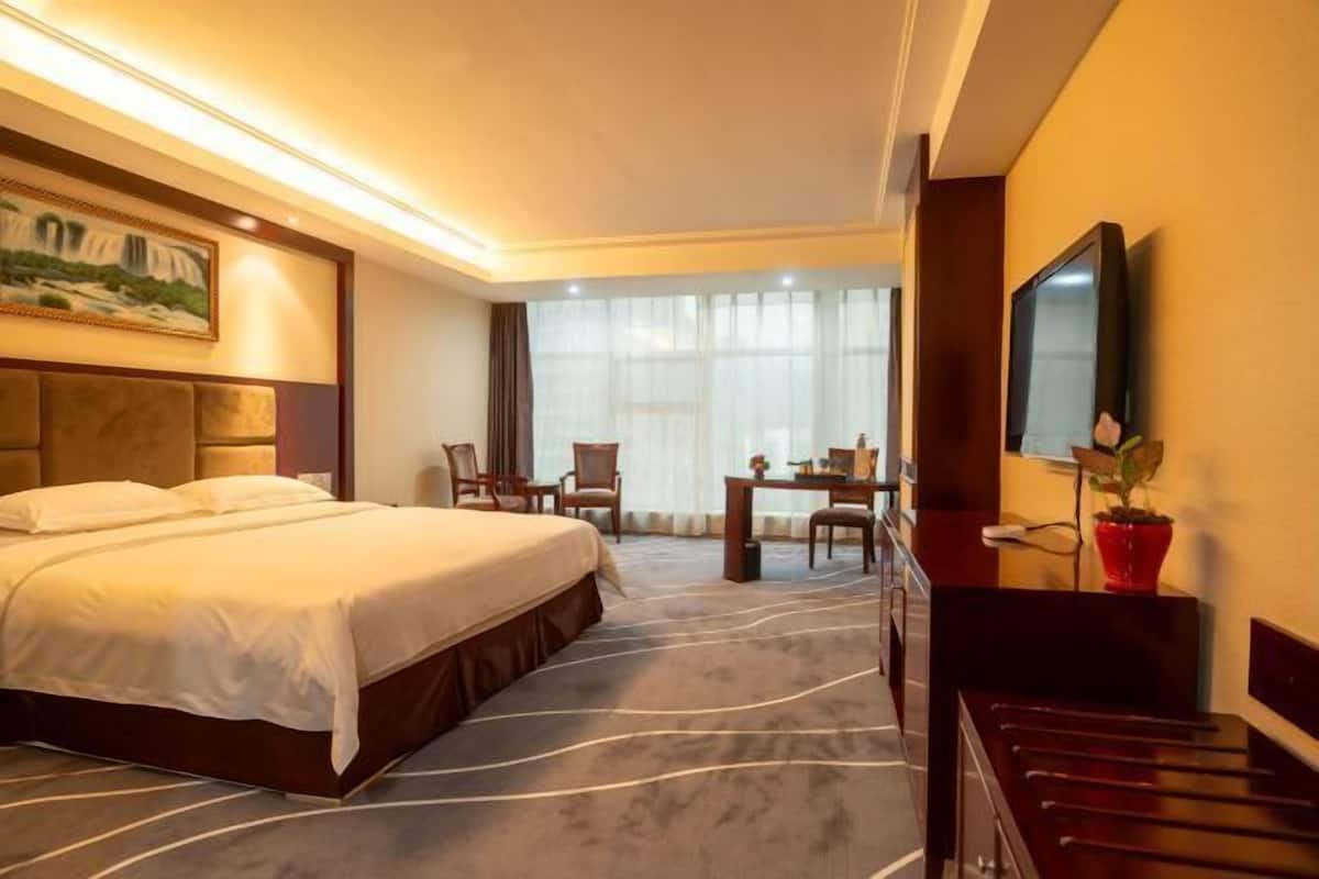 Habitación de hotel con una cama grande, un escritorio, una silla, un televisor y un cuadro en la pared.