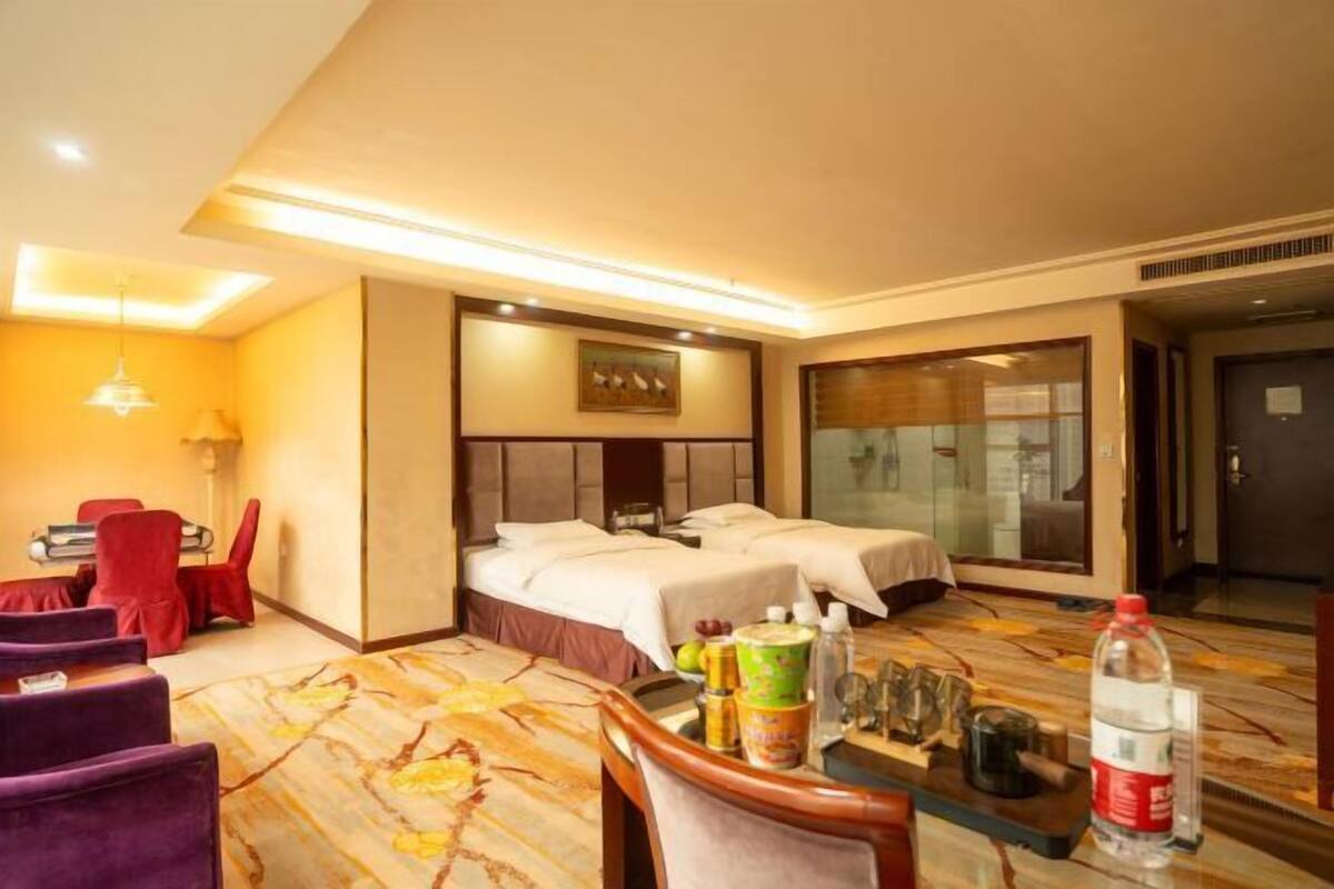 Habitación de hotel con dos camas, zona de estar con una mesa, sillas y un sofá.