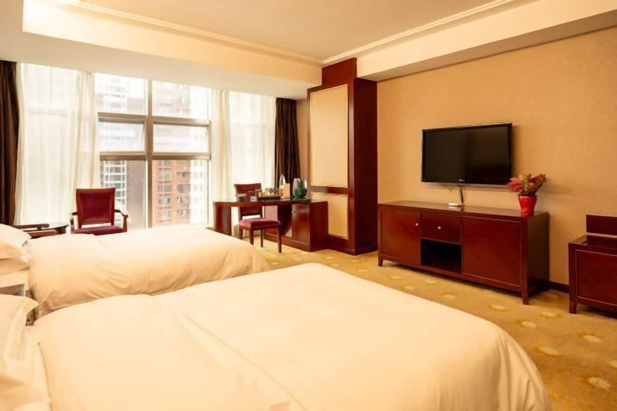 Habitación de hotel con dos camas, televisión, escritorio y ventana con cortinas.