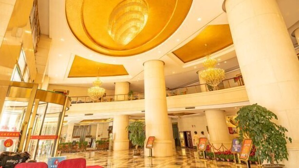 A spacious lobby with high ceilings, large columns, and a central chandelier.