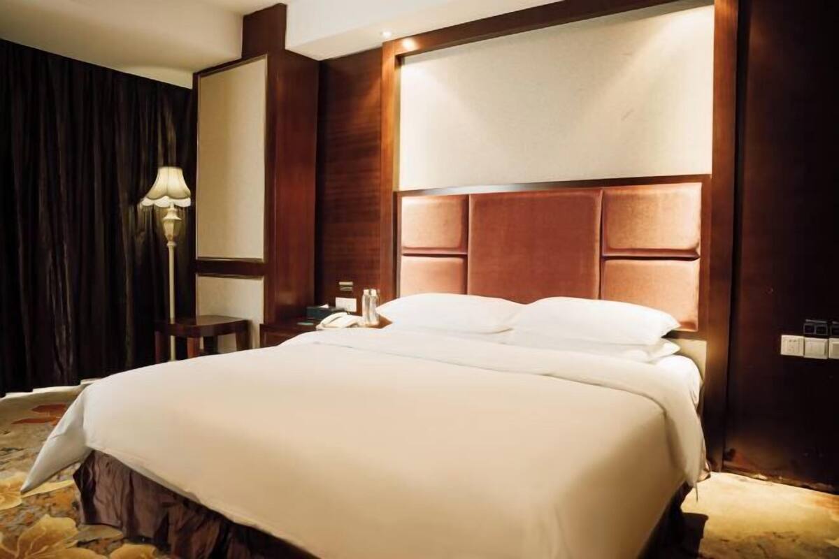 Una habitación de hotel con una cama grande, una mesita de noche, una lámpara y una cortina oscura.