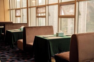 Filas de mesas de comedor con manteles verdes y sillas marrones en una habitación con ventanas amplias y una alfombra estampada.
