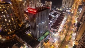 A high-rise building with illuminated signage, surrounded by other tall buildings and busy streets at night.