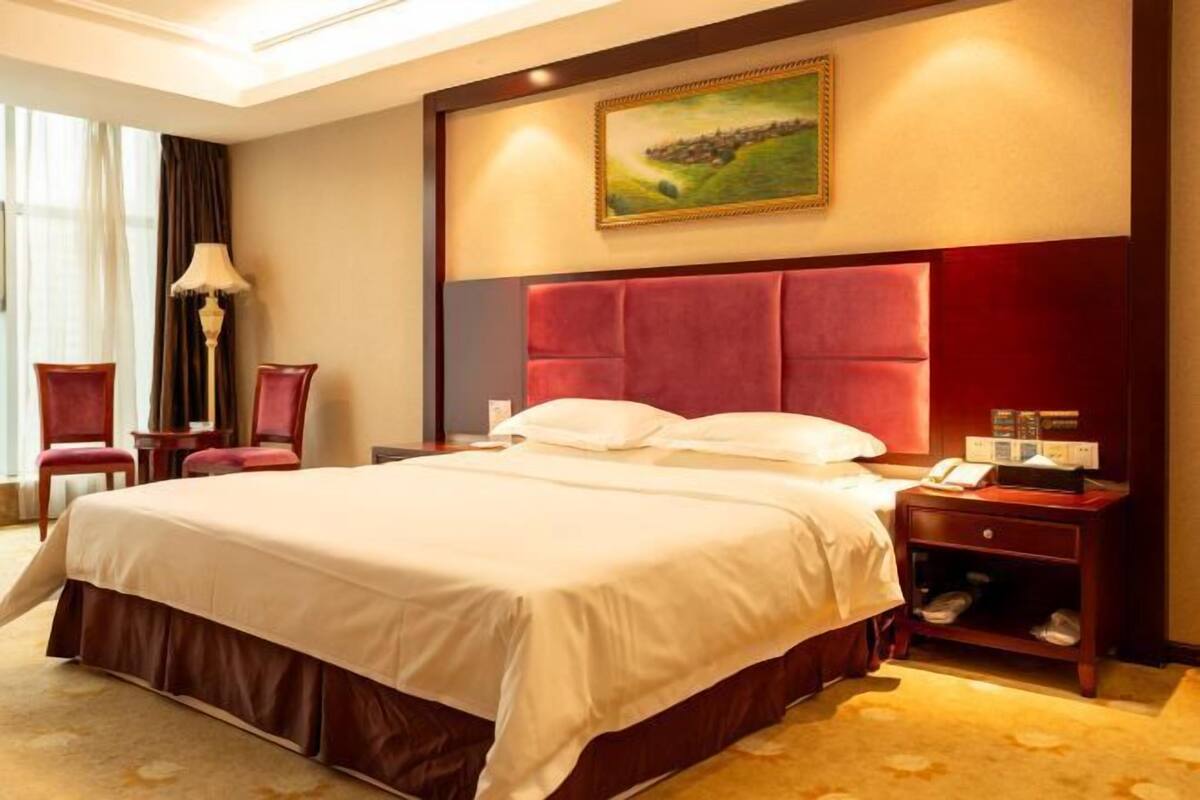Una habitación de hotel con una cama grande, una mesita de noche con una lámpara y un cuadro en la pared.