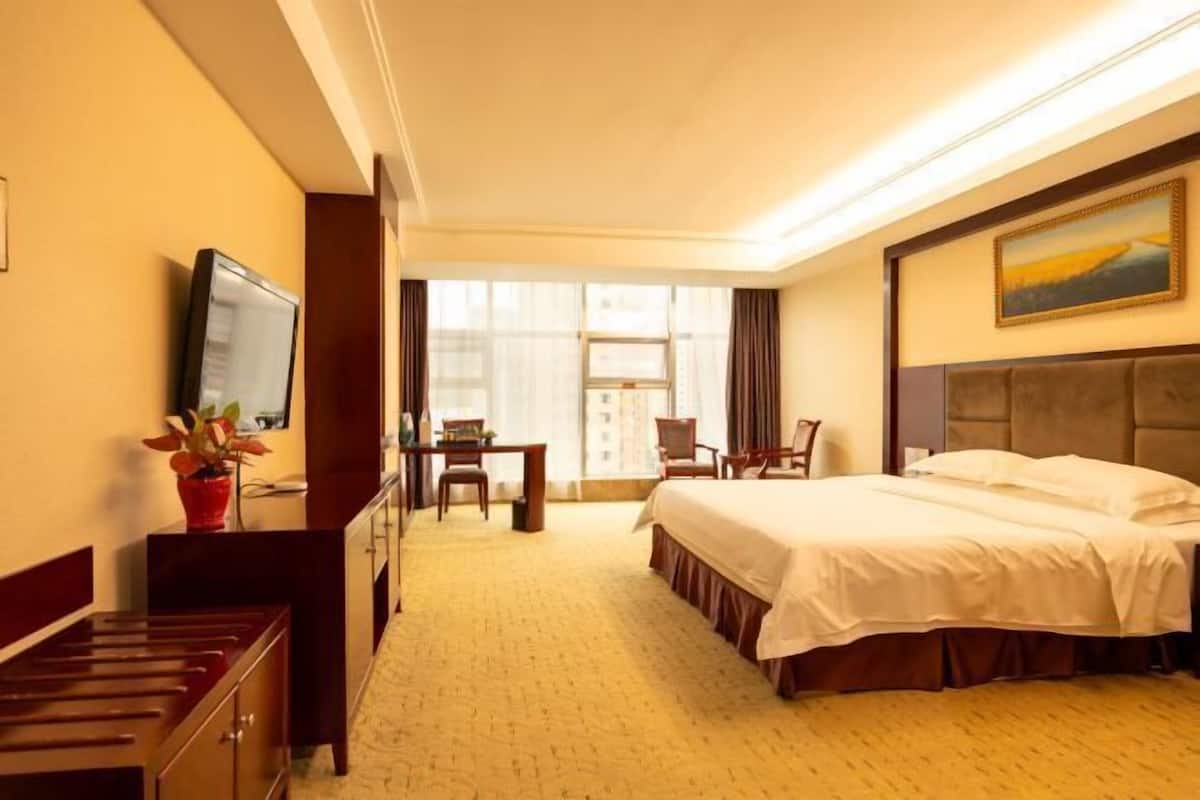 Una habitación de hotel con cama, escritorio, silla, televisor y ventana.