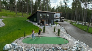 Una casa moderna con una amplia terraza, un campo de práctica de golf y barcos estacionados afuera.