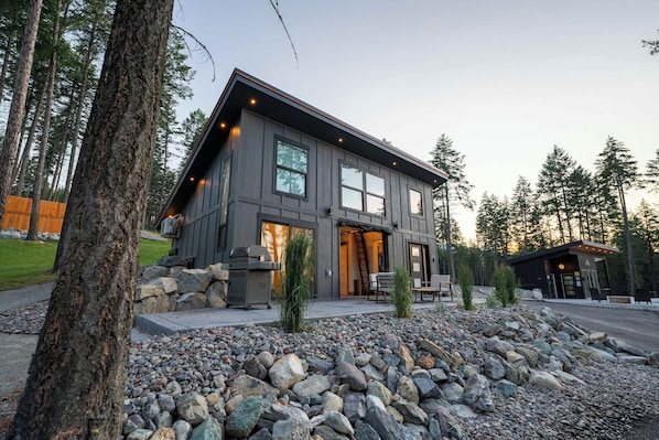 A modern two-story house with a stone foundation, large windows, and a patio area.