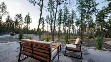 An outdoor seating area with a bench and a table, surrounded by tall trees.