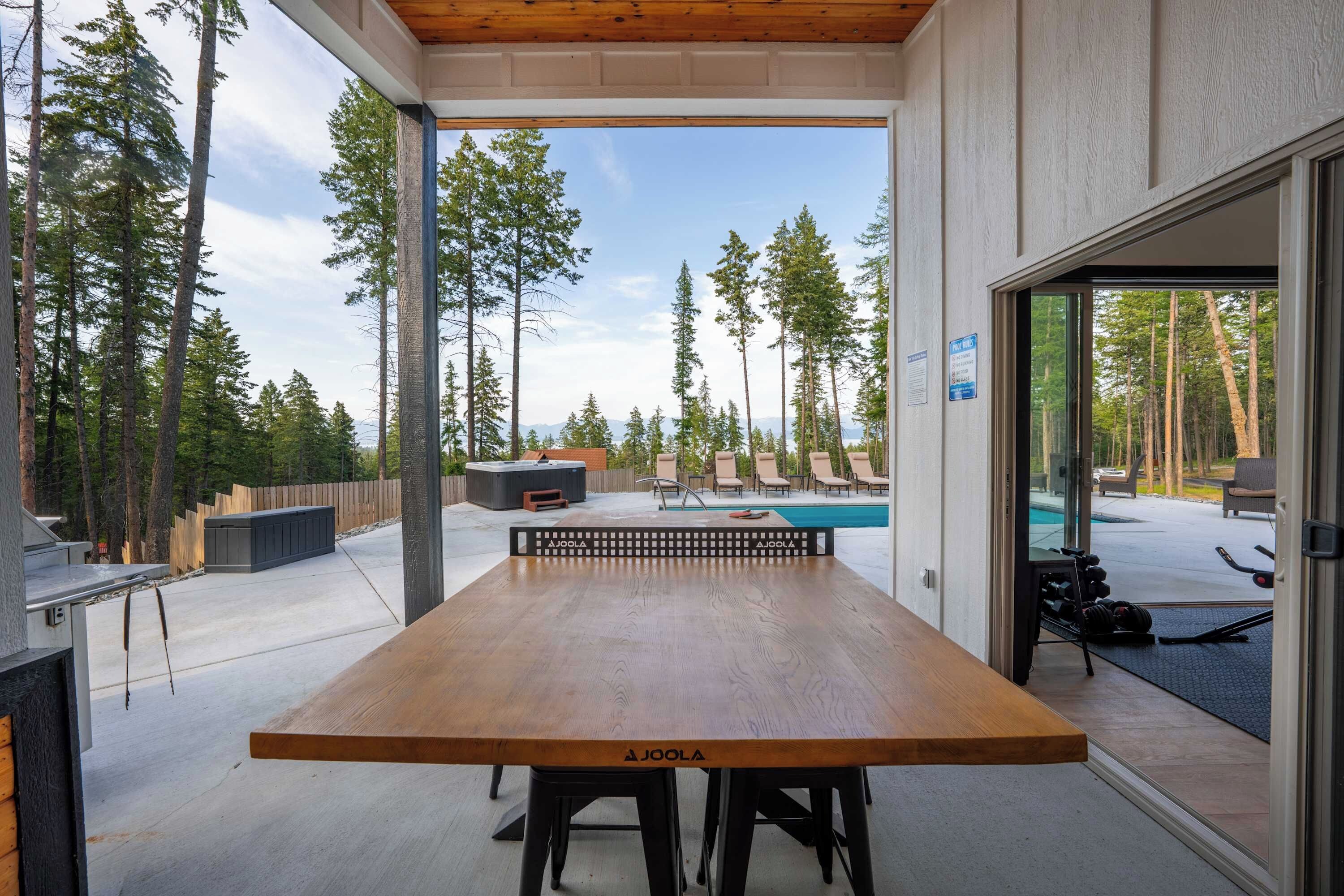 An outdoor dining area with a wooden table and chairs, a hot tub, and a poolside seating area with lounge chairs.