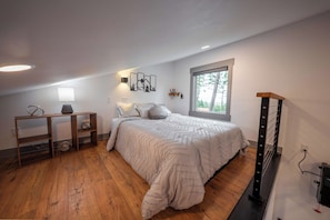 A bedroom with a bed, a nightstand, a lamp, a wall-mounted shelf, and a window with a view of trees.