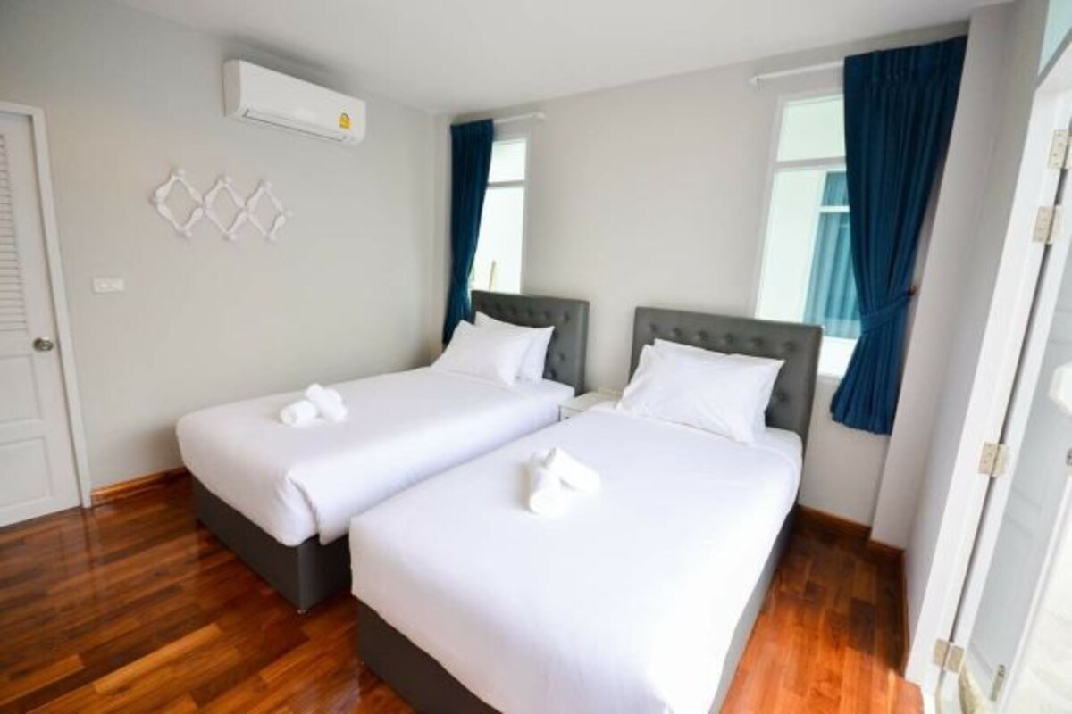 Una habitación de hotel con dos camas, un equipo de aire acondicionado blanco, piso de madera y una ventana con cortinas azules.