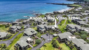 An aerial view of Kapalua Bay Villas 32B4, featuring a coastal setting with multiple villas, roads, and greenery.