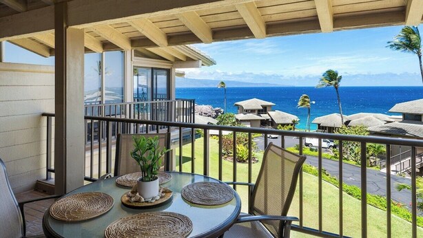 A balcony with a table set for dining, overlooking a beach with palm trees and a view of the ocean.