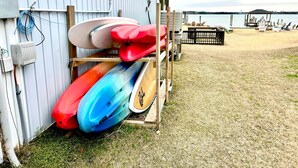Een gebouw met kajaks die buiten staan, een strand met stoelen en uitzicht op het water.