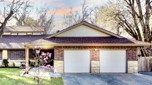 Ein zweistöckiges Haus mit Garage, Ziegelfassade und einem kleinen Vorgarten mit blühenden Pflanzen.