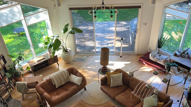 A spacious living room with two brown leather sofas, a coffee table, and a large window offering a view of a garden.