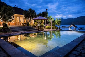 A poolside area with a clear view of the water, a covered seating area, and steps leading to a building.