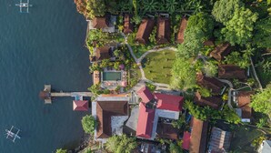 An aerial view of a coastal property with multiple buildings, a swimming pool, and a dock with a boat. - Solitude Lembeh Resort (Bitung)