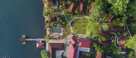 An aerial view of a coastal property with multiple buildings, a swimming pool, and a dock with a boat.