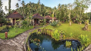 A tropical resort with multiple bungalow-style buildings, a stone pathway, and a pond with koi fish. - Solitude Lembeh Resort (Bitung)