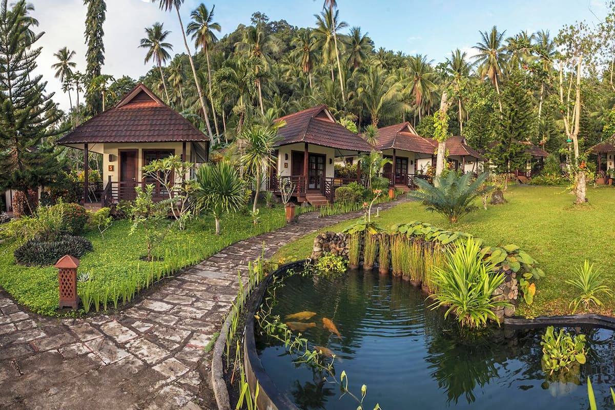 Un resort tropical con varias construcciones tipo bungaló, un sendero de piedra y un estanque con peces koi.