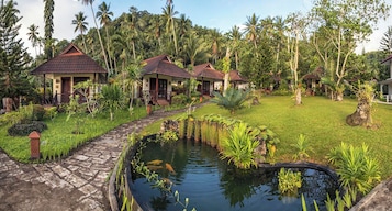 A tropical resort with multiple bungalow-style buildings, a stone pathway, and a pond with koi fish.