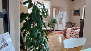 Una stanza con pavimento in legno, una sedia bianca, un letto con coperta a pois, una pianta verde grande e un armadio bianco.