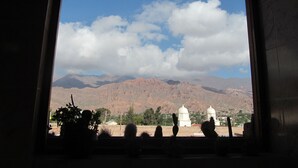 Una vista attraverso una finestra che mostra una catena montuosa sullo sfondo, cielo sereno e vegetazione in primo piano.