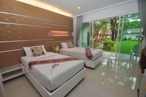 A modern hotel room with two beds, a large sliding glass door to a garden, and a view of the outdoors. - Phi Phi Rimlay Resort (Phi Phi Islands)
