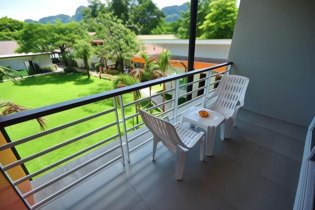 Un balcon donnant sur une pelouse verdoyante et des arbres, deux chaises en plastique blanches et une petite table sur laquelle se trouve un bol orange.