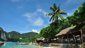A beach with boats, a palm tree, and a thatched-roof building. - Phi Phi Rimlay Resort (Phi Phi Islands)