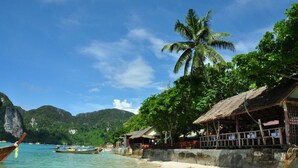 A beach with boats, a palm tree, and a thatched-roof building. - Phi Phi Rimlay Resort (Phi Phi Islands)