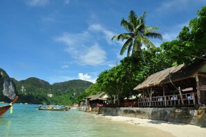 A beach with boats, a palm tree, and a thatched-roof building. - Phi Phi Rimlay Resort (Phi Phi Islands)