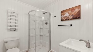 Et badeværelse med en glasvæg omkring brusebadet, et toilet og en vask med et moderne vandhaner.