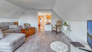 A spacious living room with a high ceiling, a cozy sofa, a wooden chest, and a small round rug.
