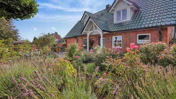 A house with a green roof, brick walls, and a garden with various flowers.