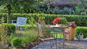 A garden patio with a table and chairs, surrounded by various plants and flowers.