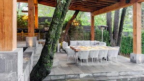 An outdoor patio with a wooden pergola, stone flooring, and a round table with white chairs. - Forest Guesthouse Avándaro, entertainment and comfort for adults and children (Valle de Bravo)
