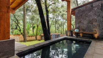 A swimming pool with a stone wall and wooden pergola, surrounded by trees.